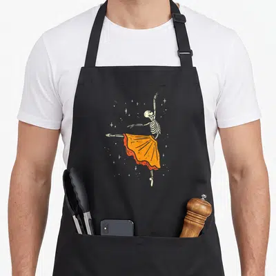 Dancing halloween apron - Skeleton ballerina in orange tutu surrounded by distressed white stars — shown on a black cotton canvas apron against a white background
