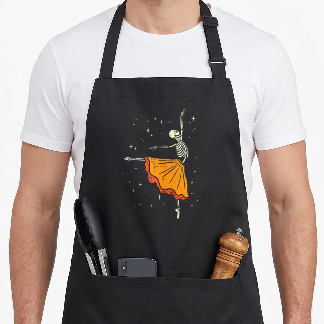 Dancing halloween apron - Skeleton ballerina in orange tutu surrounded by distressed white stars — shown on a black cotton canvas apron against a white background