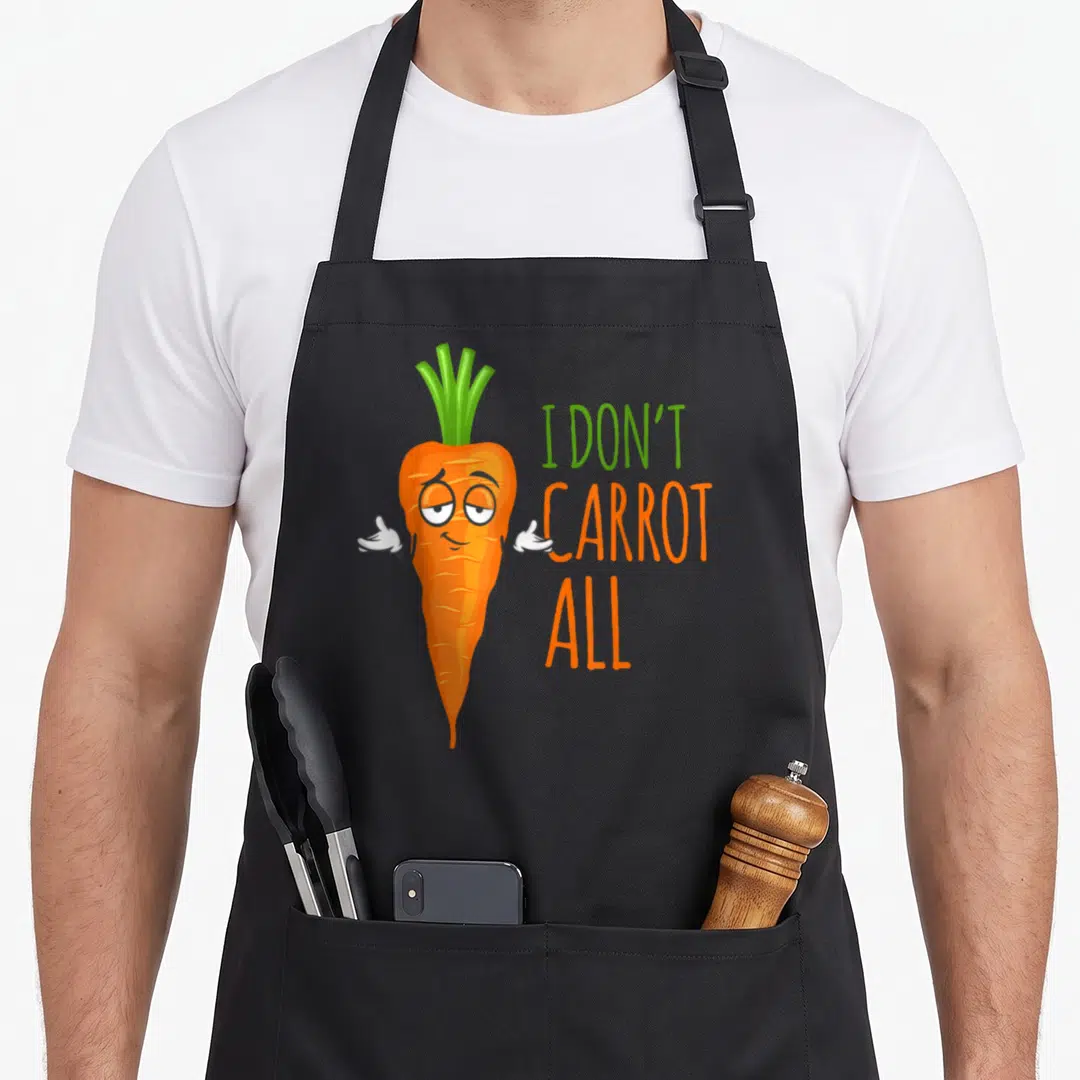 Carrot vegan apron - Cartoon orange carrot shrugging next to stacked I Don't Carrot All text — shown on a black cotton canvas apron against a white background