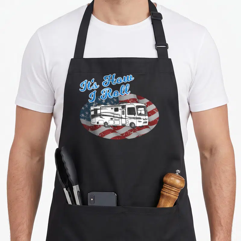 Motorhome camping apron - Arched text It's How I Roll above an RV on a distressed circular flag background — shown on a black cotton canvas apron against a white background