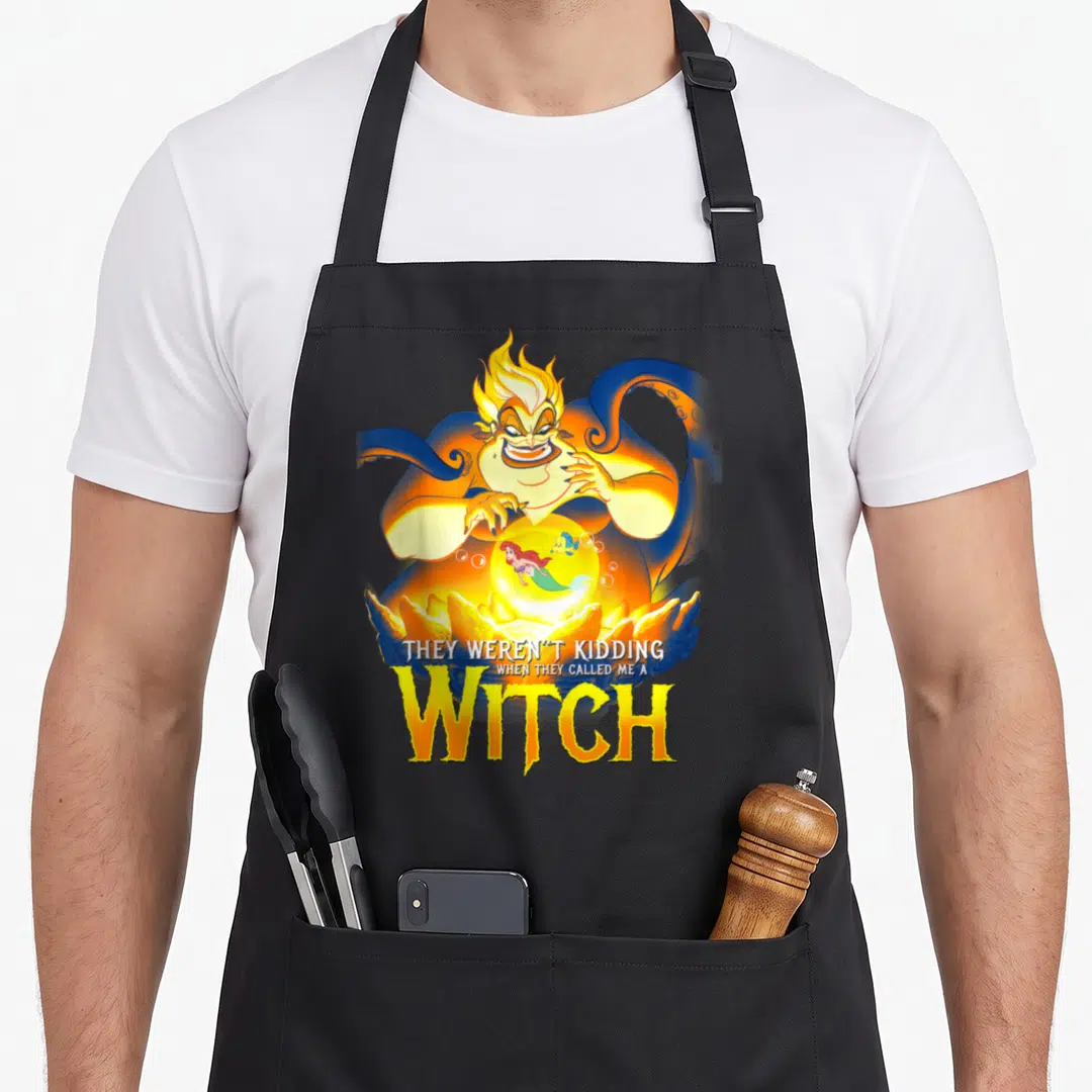 Evil witch apron - Sea witch holding glowing orb with mermaid and fish, stacked yellow WITCH text below — shown on a black cotton canvas apron against a white background
