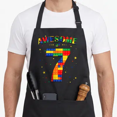 Building block & apron - Colorful toy brick number 7 with AWESOME at text and scattered stars — shown on a black cotton canvas apron against a white background