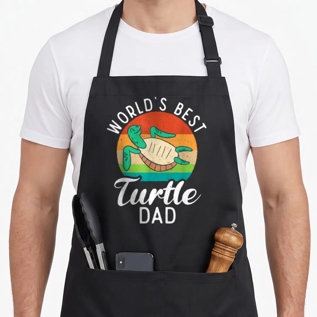 Turtle hummingbird dad apron - Retro striped sun with cartoon turtle and text WORLD'S BEST Turtle DAD — shown on a black cotton canvas apron against a white background