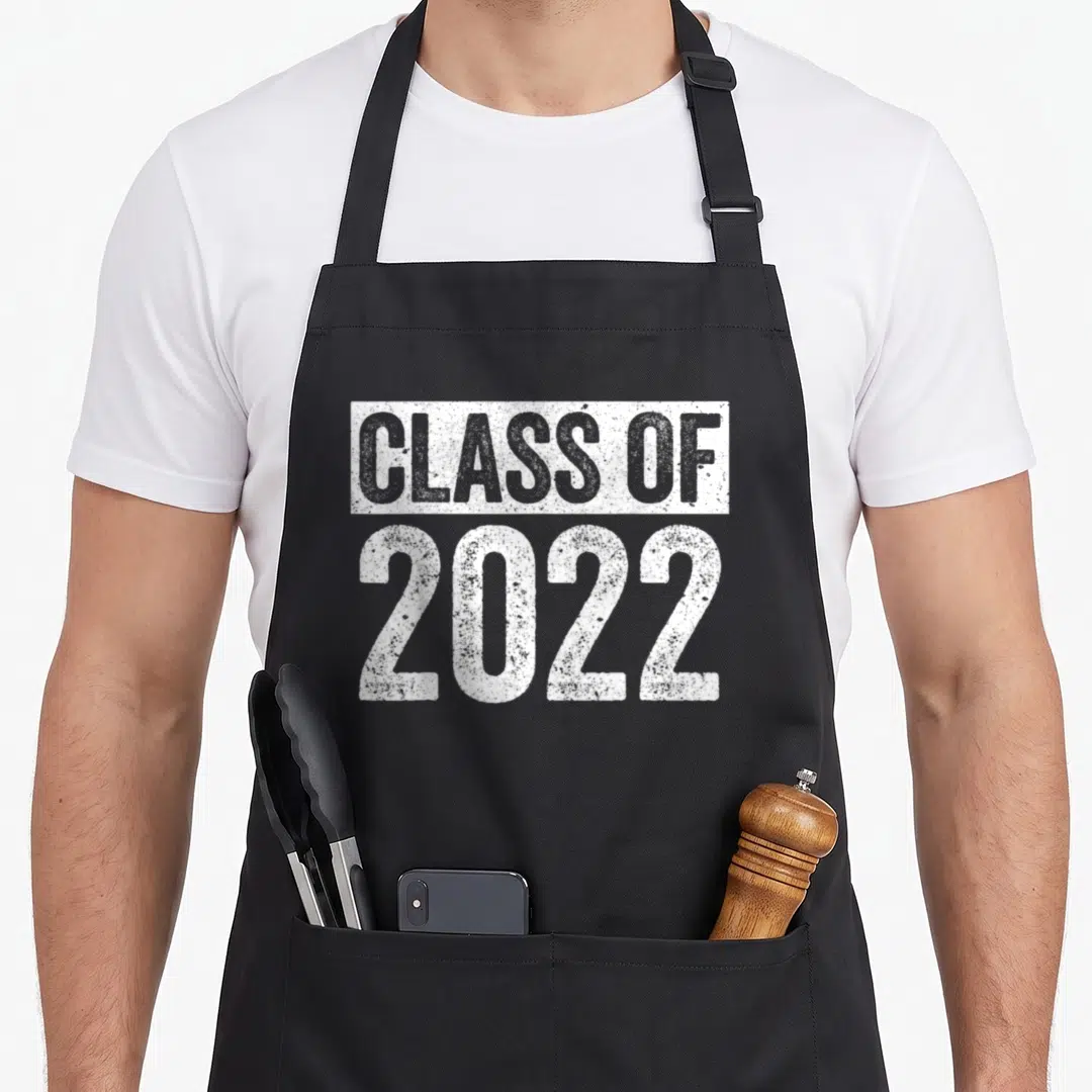 Graduate future class apron - White distressed text reading CLASS OF 2022 stacked on grey background — shown on a black cotton canvas apron against a white background