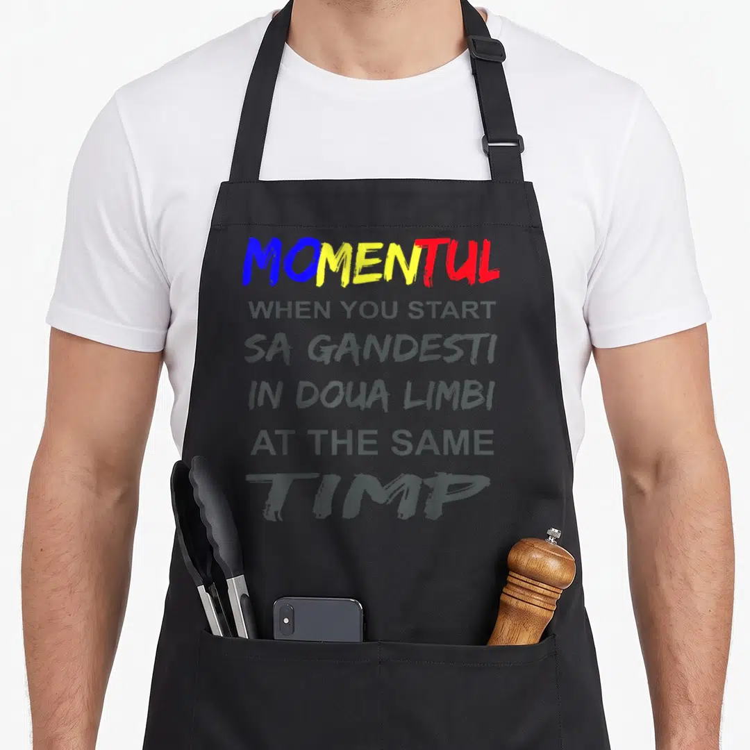 Romania romanian apron - Stacked bilingual text MOMENTUL in blue yellow red grey on grey background — shown on a black cotton canvas apron against a white background