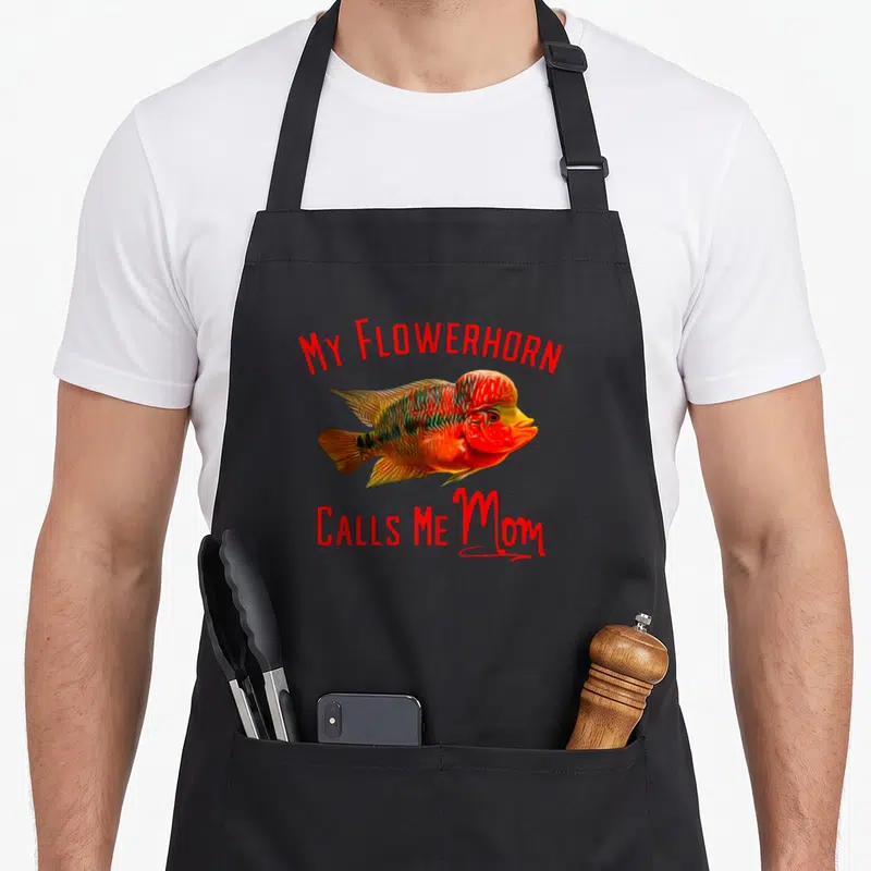 Flowerhorn mother's apron - Realistic red orange flowerhorn fish with MY FLOWERHORN CALLS ME Mom text — shown on a black cotton canvas apron against a white background
