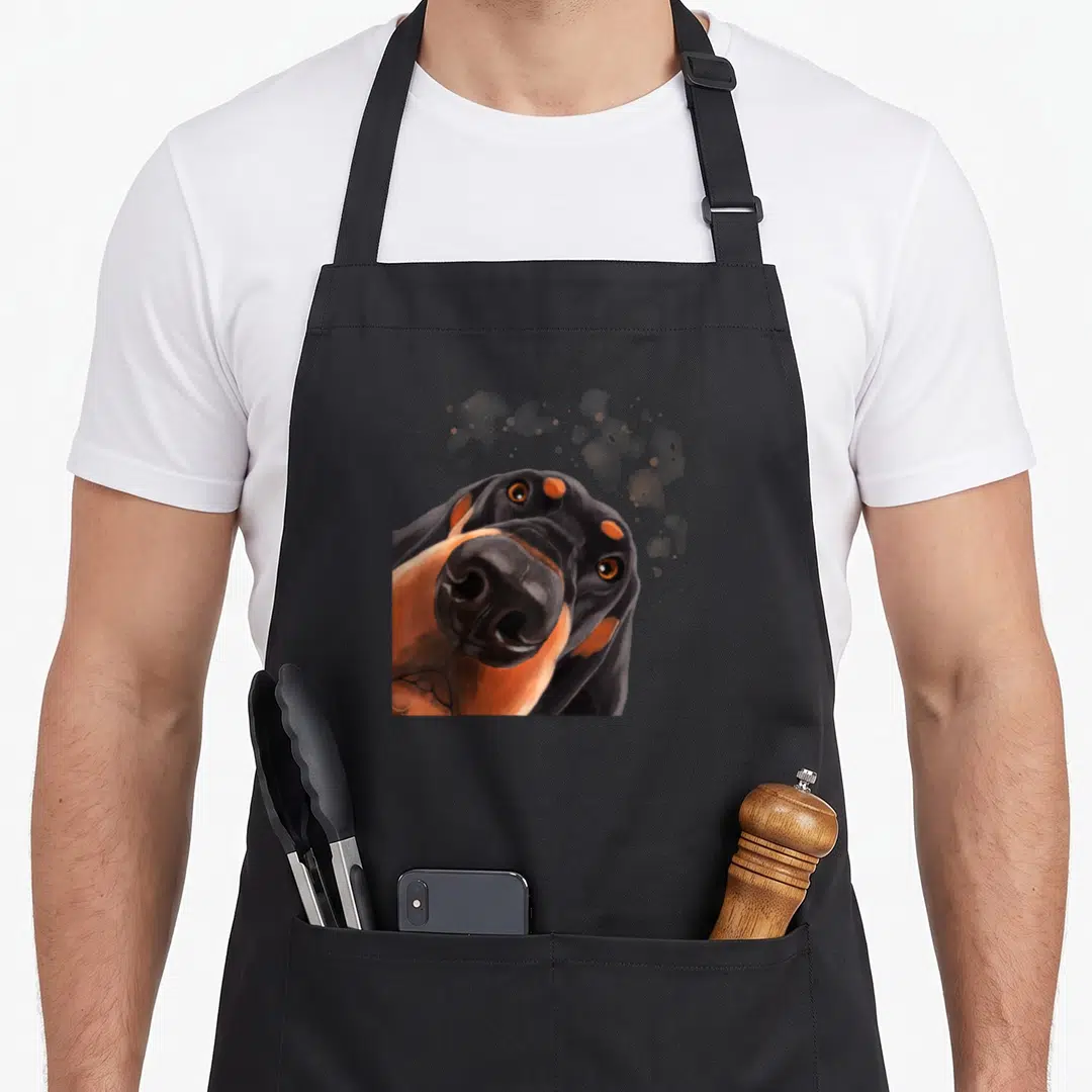 Curious coonhound dog apron - Realistic black tan and grey hound face with artistic paint splatters floating above — shown on a black cotton canvas apron against a white background