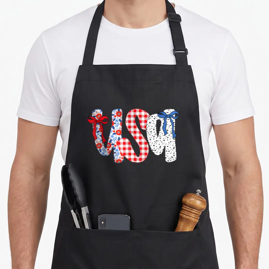 Bow 4th of july apron - Patterned usa text with red floral, gingham, and speckled fills plus red and blue bows — shown on a black cotton canvas apron against a white background