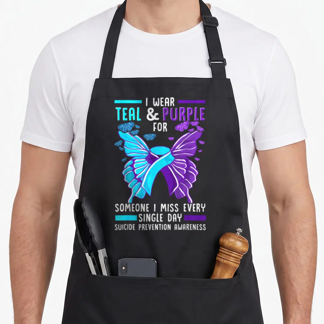 Suicide prevention ribbon apron - Teal and purple ribbon butterfly with I WEAR TEAL PURPLE text — shown on a black cotton canvas apron against a white background