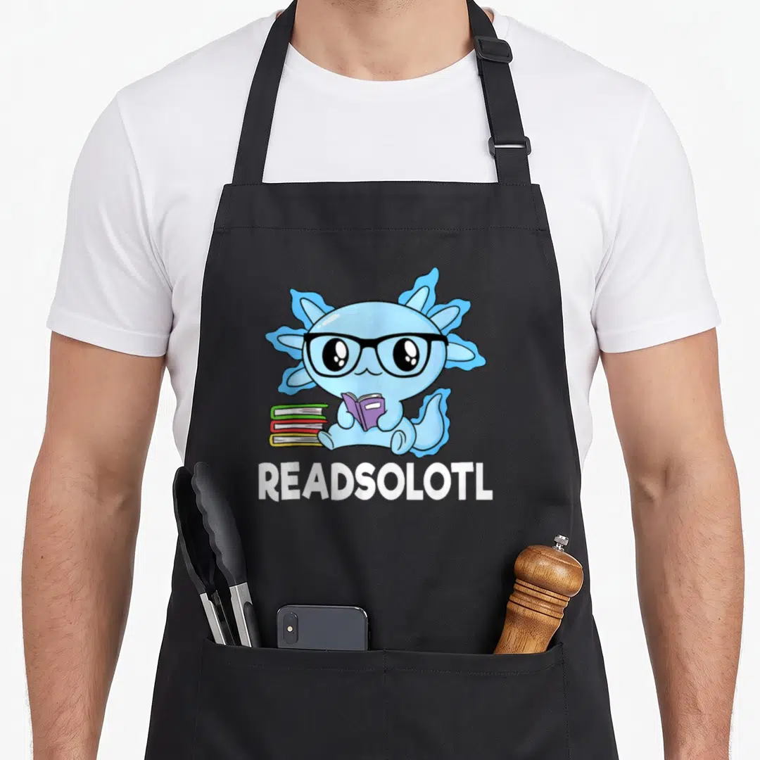 Readsolotl kawaii apron - Blue cartoon axolotl with glasses holding purple book next to stack with white text below — shown on a black cotton canvas apron against a white background