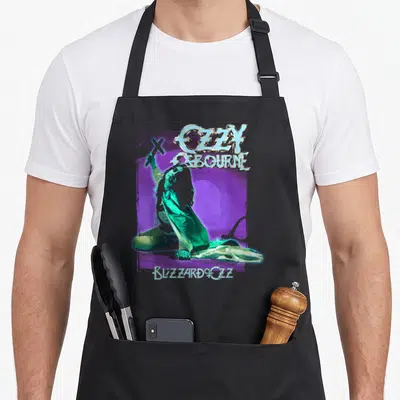 Osbourne pastel aprons - Ozzy Osbourne kneeling holding cross purple green silver Blizzard of Ozz text — shown on a black cotton canvas apron against a white background