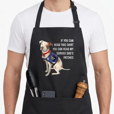 Read service apron - Cartoon white and brown dog in blue vest next to five lines of white text about reading patches — shown on a black cotton canvas apron against a white background