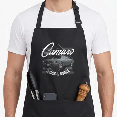 Camaro muscle apron - White Camaro car illustration with script text and diamond line background — shown on a black cotton canvas apron against a white background