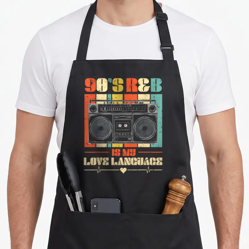 90s music r aprons - Retro boombox over orange, yellow, teal, grey stripes with 90'S R&B text and heartbeat line — shown on a black cotton canvas apron against a white background