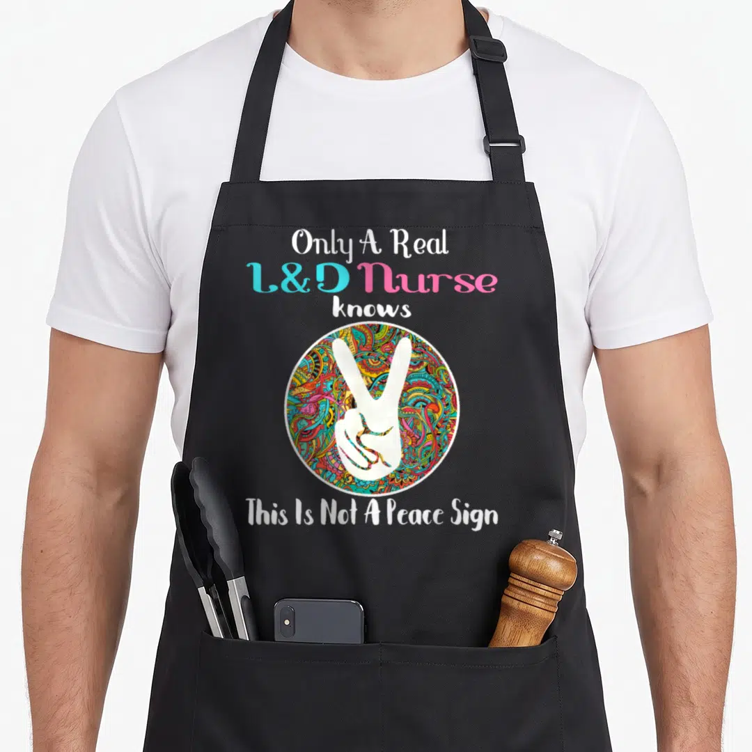 Birth nurse apron - White V-sign hand on multicolored circle with L&D nurse text — shown on a black cotton canvas apron against a white background