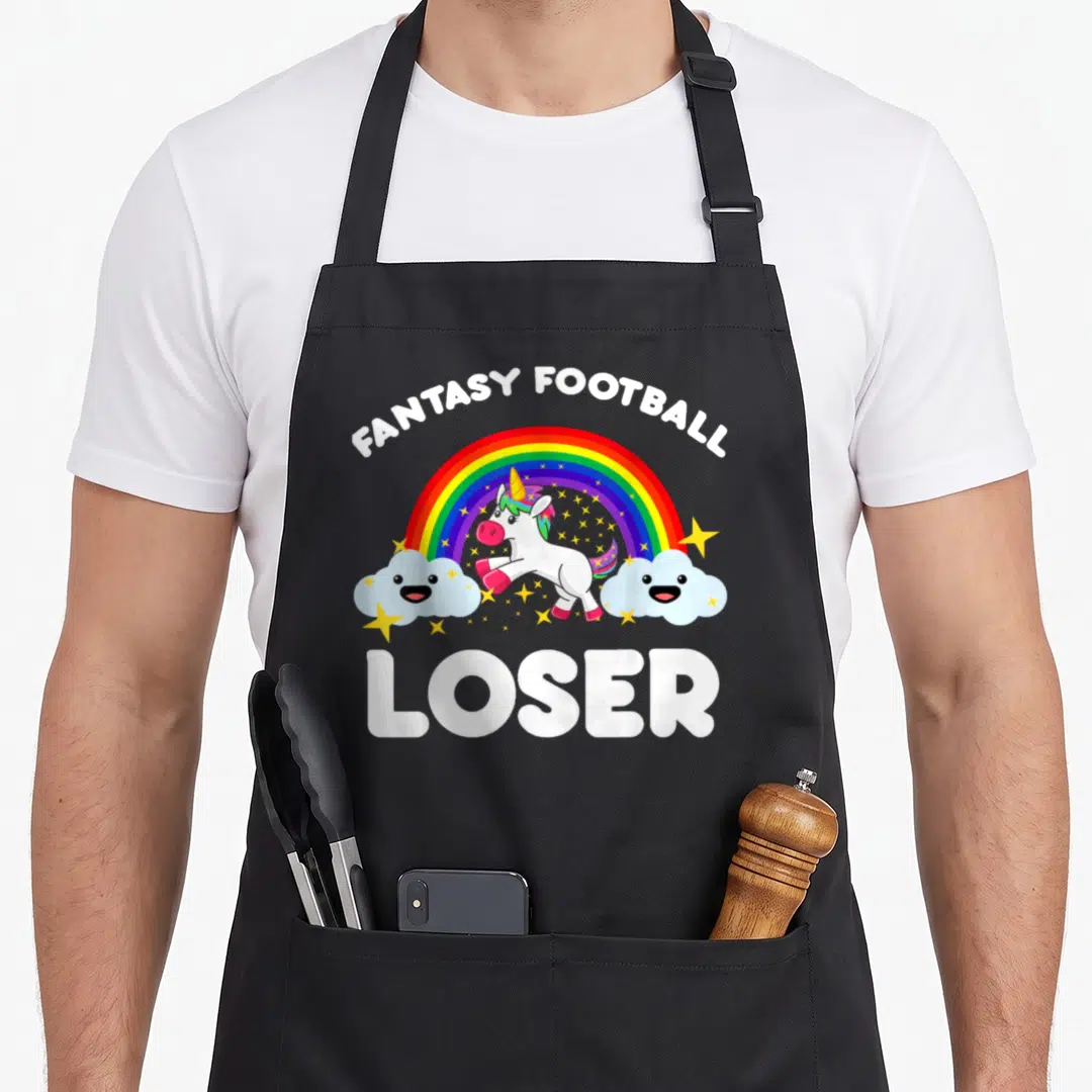 Trophy football apron - Cartoon unicorn under rainbow with Fantasy Football Loser text and smiling clouds — shown on a black cotton canvas apron against a white background