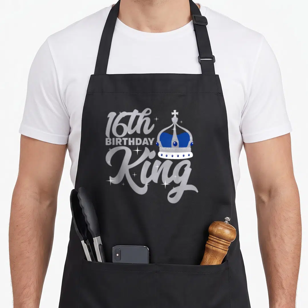 16th kings apron - Silver crown with blue accents next to stacked 16th BIRTHDAY King text and white sparkles — shown on a black cotton canvas apron against a white background