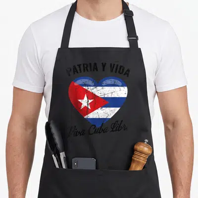 Patria cuba apron - Distressed heart containing Cuban flag with arched black text PATRIA Y VIDA Viva Cuba Libre — shown on a black cotton canvas apron against a white background