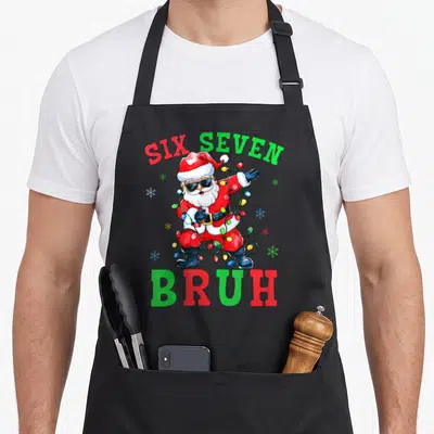 Six seven christmas santa apron - Cartoon Santa wrapped in lights with text six seven bruh — shown on a black cotton canvas apron against a white background