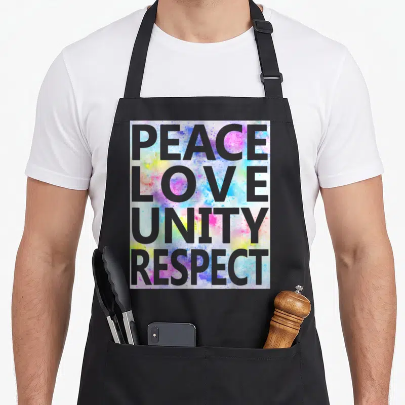 Rave dubstep apron - Grey PEACE LOVE UNITY RESPECT text over pink blue yellow green watercolor splatter — shown on a black cotton canvas apron against a white background