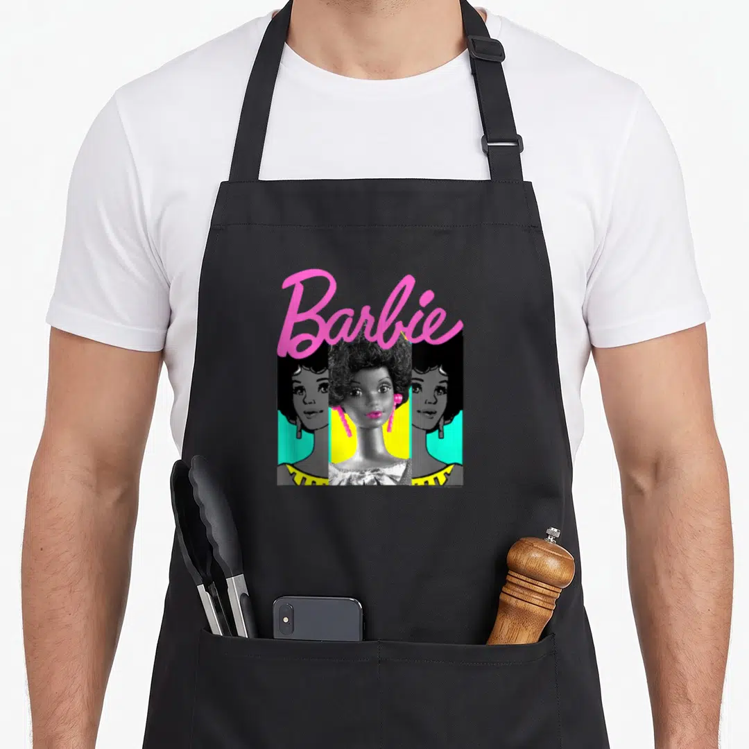 Afro barbiecore apron - Three pop-art woman portraits under pink arched Barbie text in pink black yellow cyan — shown on a black cotton canvas apron against a white background