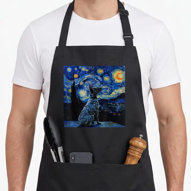 Starry dog kitchen apron - Blue heeler sitting in swirling blue night sky with yellow stars and cypress tree — shown on a black cotton canvas apron against a white background