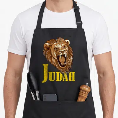 Roar lion apron - Realistic brown lion head above yellow JUDAH text with cracked texture — shown on a black cotton canvas apron against a white background