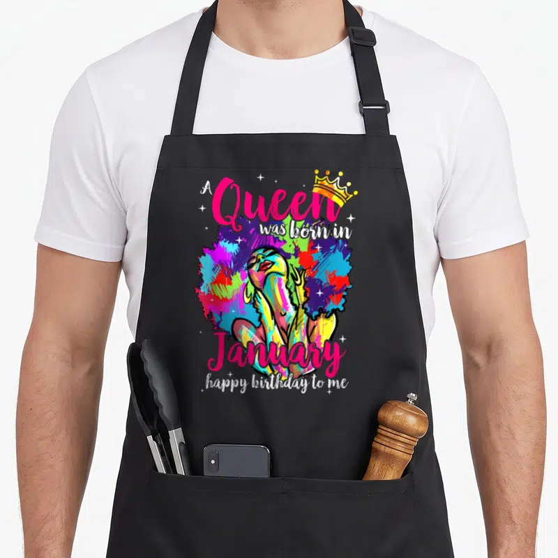 Dashiki birthday apron - Multicolored woman with afro and crown surrounded by pink and white text celebrating a January — shown on a black cotton canvas apron against a white background