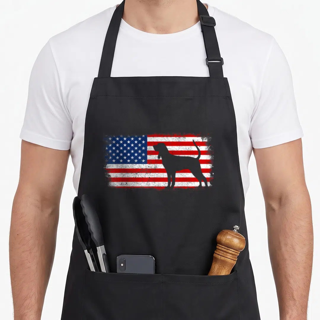 Coonhound dog breed apron - White dog silhouette standing on a distressed red white and blue American flag graphic — shown on a black cotton canvas apron against a white background
