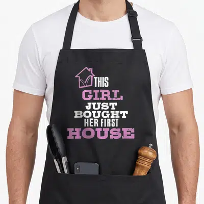 Homeowner bought novelty apron - Pink house outline with checkmark and stacked white and pink distressed text reading — shown on a black cotton canvas apron against a white background
