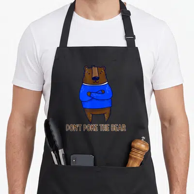 Vintage poke apron - Cartoon brown bear in blue shirt with crossed arms above text DON'T POKE THE BEAR — shown on a black cotton canvas apron against a white background