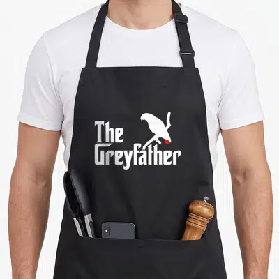 Greyfather bird apron - White parrot silhouette with red tail above stacked The Greyfather text — shown on a black cotton canvas apron against a white background