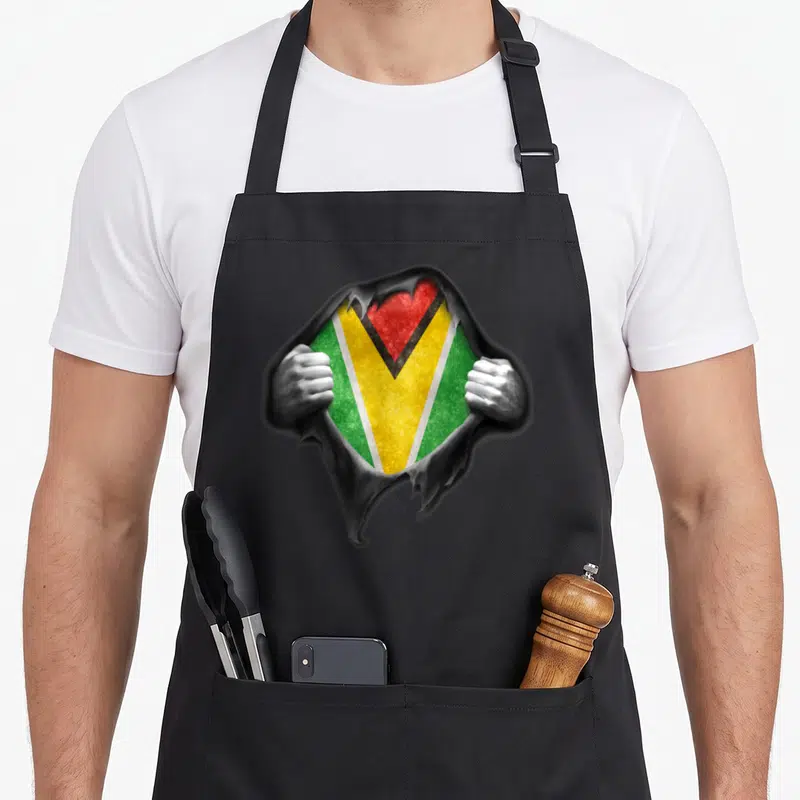 Proud guyanese apron - Flag visible through grey torn paper held by two hands in green yellow red — shown on a black cotton canvas apron against a white background