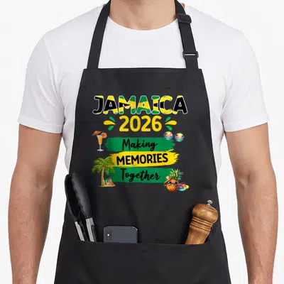 Jamaica memory apron - JAMAICA 2026 Making Memories Together text with cocktail, sunglasses, palm tree, and pineapple — shown on a black cotton canvas apron against a white background