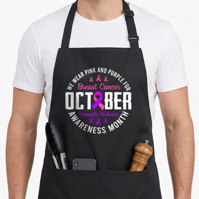 Month domestic aprons - Circular typography with pink and purple awareness ribbons and October text — shown on a black cotton canvas apron against a white background