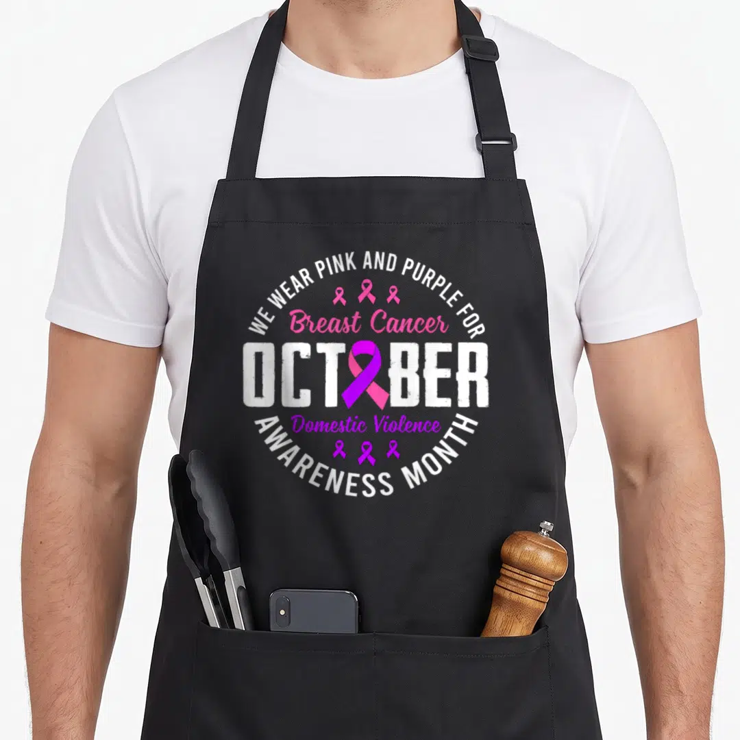Month domestic aprons - Circular typography with pink and purple awareness ribbons and October text — shown on a black cotton canvas apron against a white background