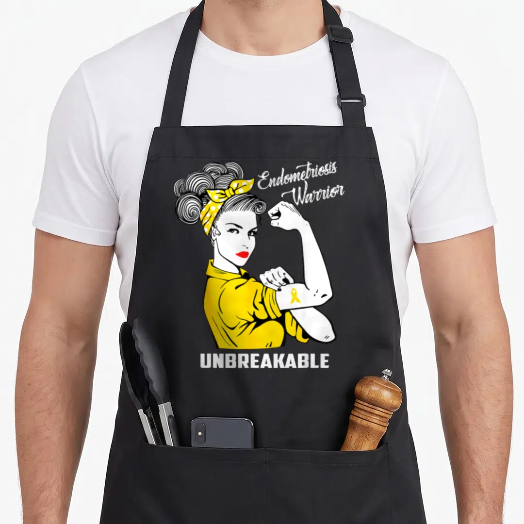 Warrior endometriosis awareness apron - Cartoon woman flexing arm with yellow ribbon and text Endometriosis Warrior — shown on a black cotton canvas apron against a white background