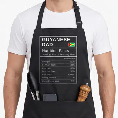 Guyanese father day apron - Nutrition facts label graphic listing Dad traits like Strength 100% and Unconditional Love — shown on a black cotton canvas apron against a white background