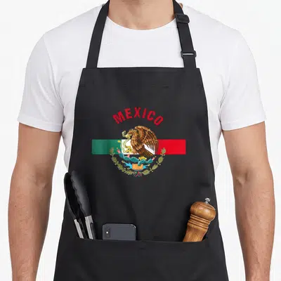 Camiseta mexico apron - Arched MEXICO text above eagle on cactus over red white and green flag — shown on a black cotton canvas apron against a white background
