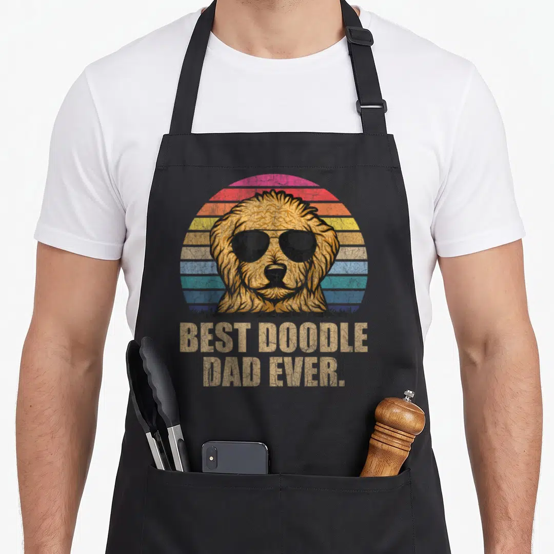 Vintage doodle goldendoodle apron - Retro dog in sunglasses with BEST DOODLE DAD EVER text on striped sun background — shown on a black cotton canvas apron against a white background