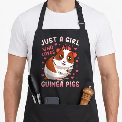 Guinea pig mom apron - Cartoon brown and white guinea pig with pink bow and hearts under arched text — shown on a black cotton canvas apron against a white background