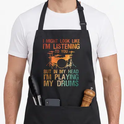 Player drum apron - Distressed orange and teal drum kit with sarcastic text about playing drums in head — shown on a black cotton canvas apron against a white background