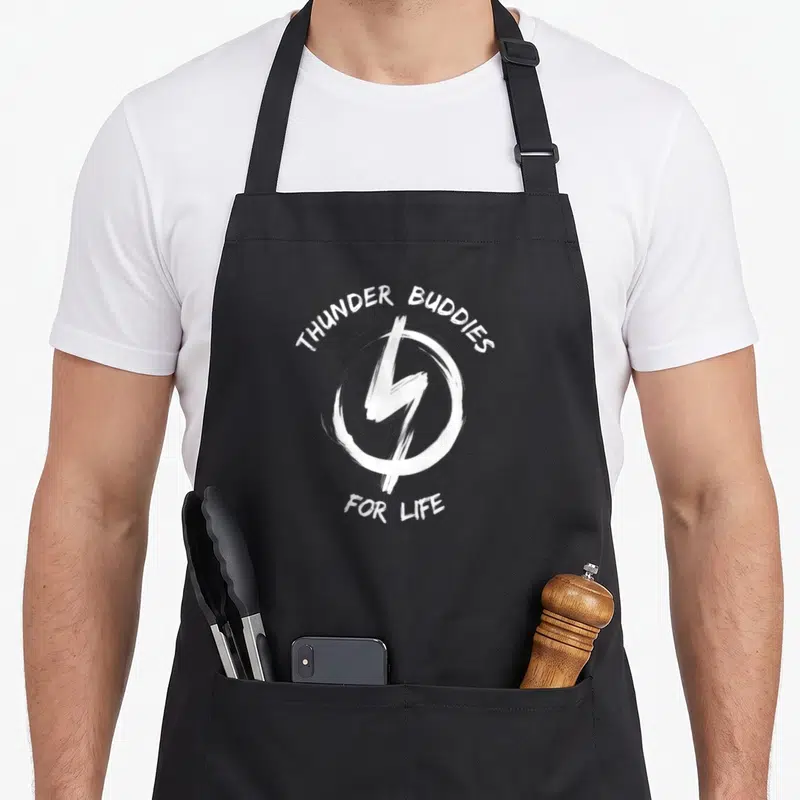 Thunder buddy aprons - White lightning bolt in brush circle with THUNDER BUDDIES FOR LIFE text — shown on a black cotton canvas apron against a white background