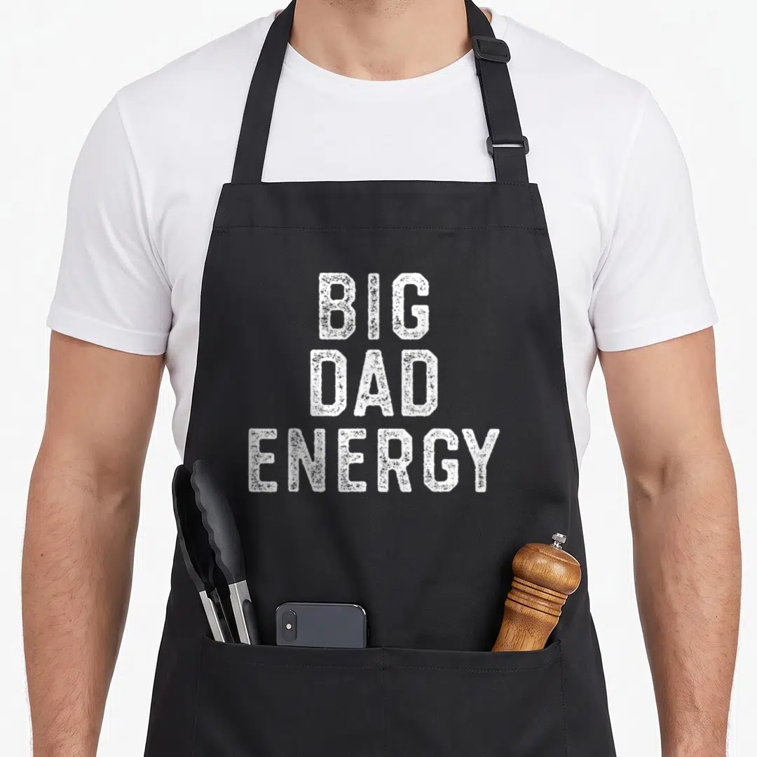 Energy gag aprons - Stacked white distressed text reading BIG DAD ENERGY — shown on a black cotton canvas apron against a white background