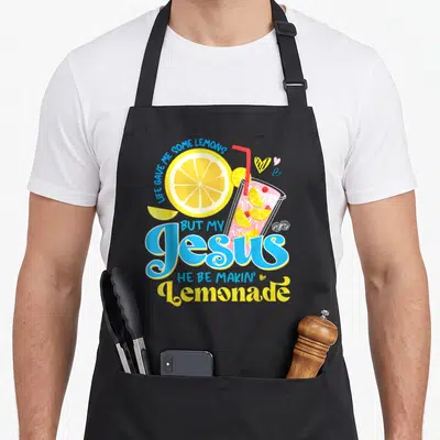But lemonade apron - LIFE GAVE ME SOME LEMONS text with pink lemonade glass and yellow slice — shown on a black cotton canvas apron against a white background