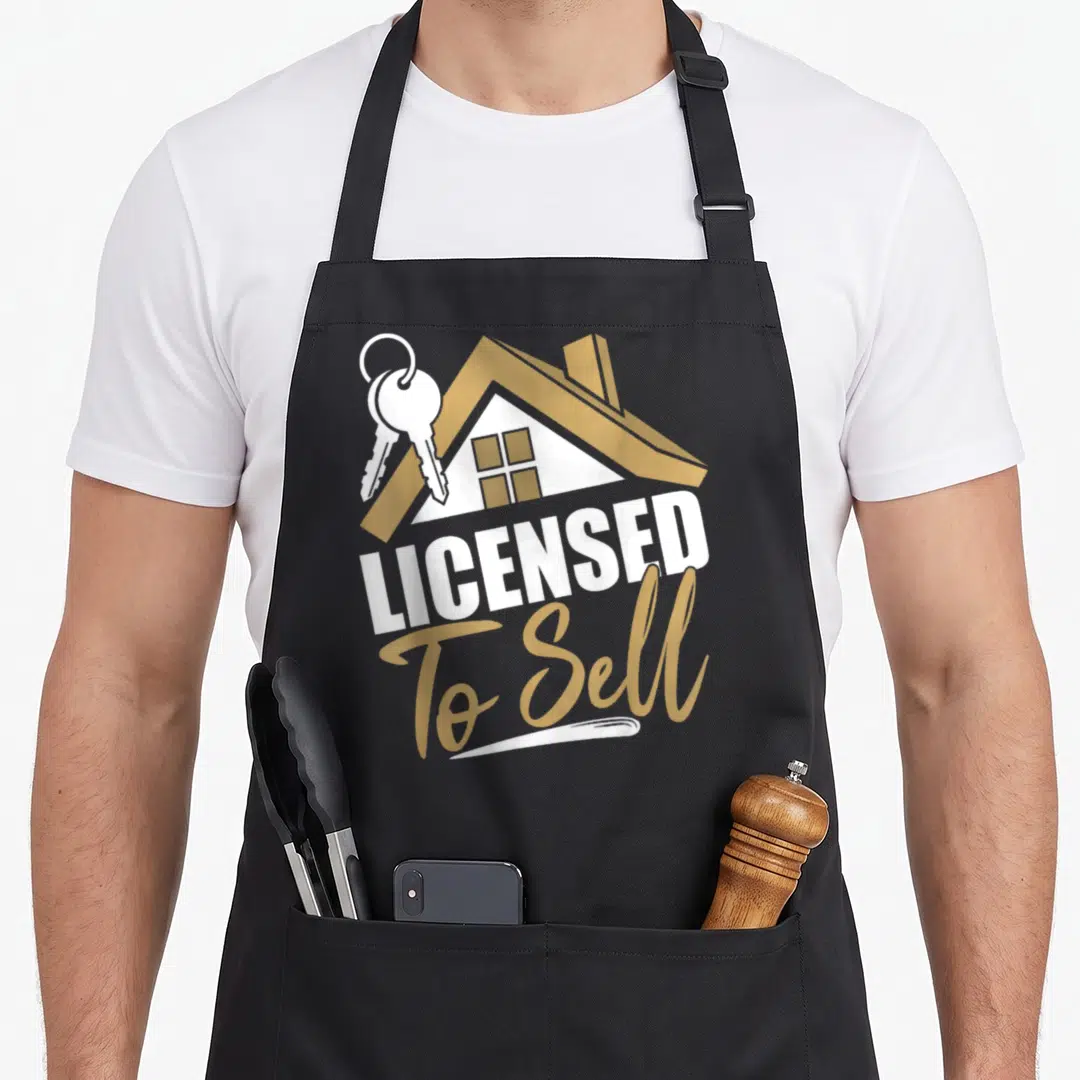 Sell realtor real estate agent apron - Gold house icon with keys above white LICENSED text and gold To Sell script — shown on a black cotton canvas apron against a white background