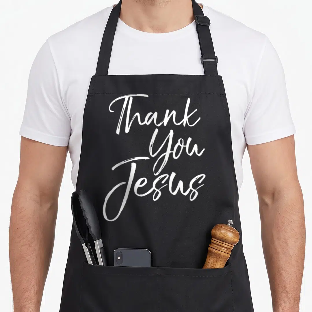 Thankfulness christian apron - White stacked script reading Thank You Jesus on black fabric — shown on a black cotton canvas apron against a white background