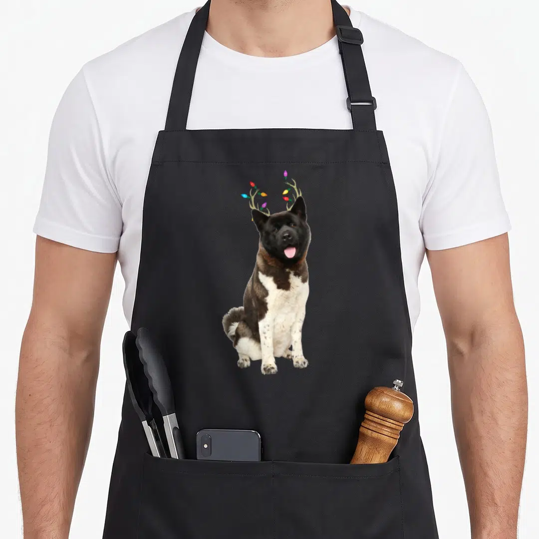 Akita reindeer christmas apron - Sitting black and white dog with green antlers and colorful Christmas lights — shown on a black cotton canvas apron against a white background