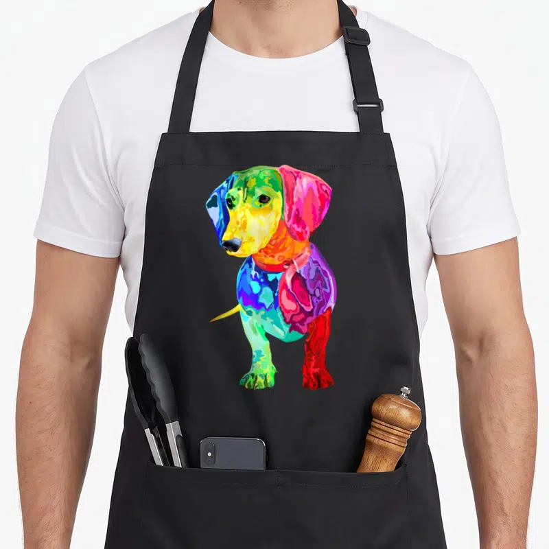 Colorful wiener apron - Multicolored pop-art dachshund with blue, green, yellow, red, purple, and pink blocks — shown on a black cotton canvas apron against a white background