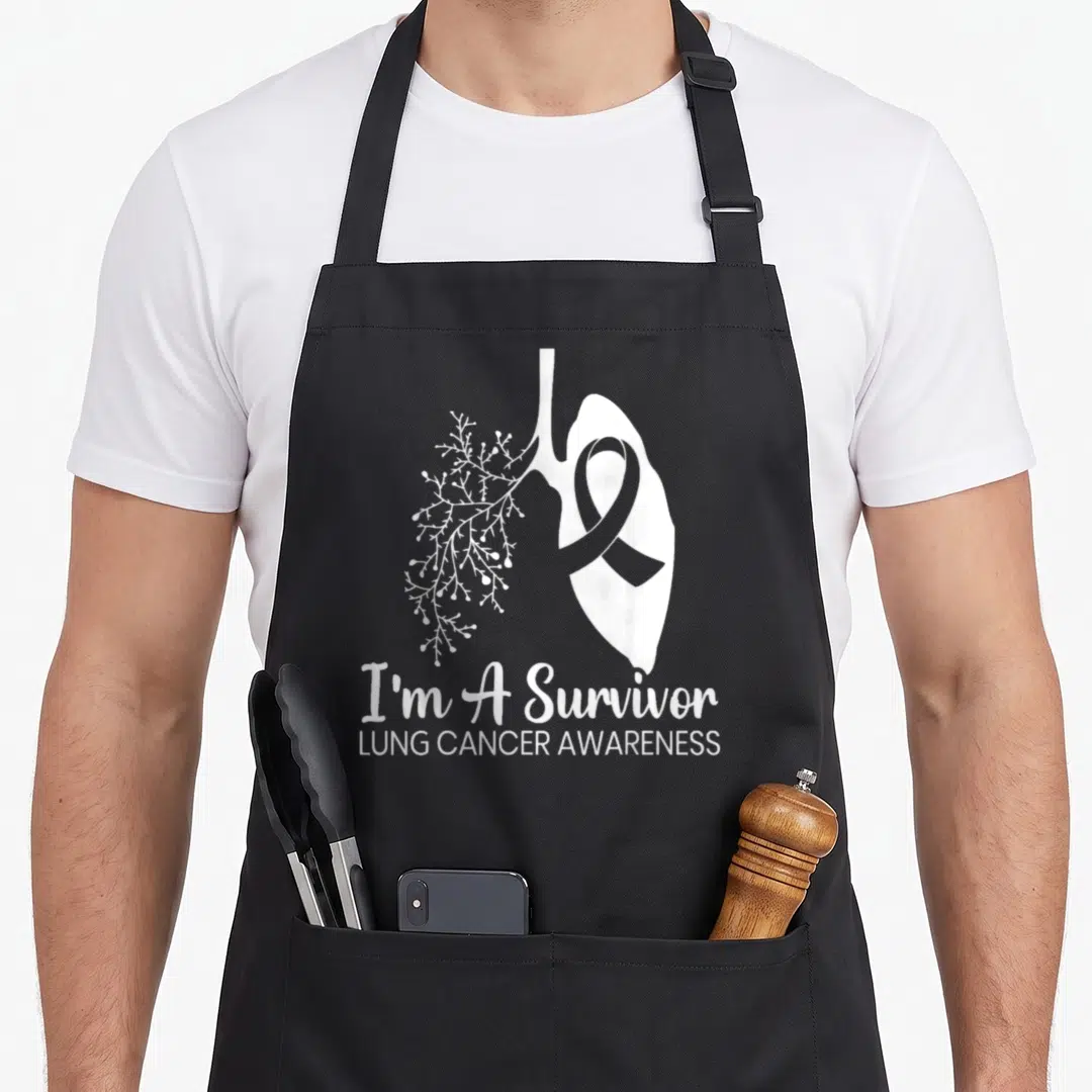 Survivor lung ribbon apron - White stylized lung with awareness ribbon and I'm A Survivor text — shown on a black cotton canvas apron against a white background